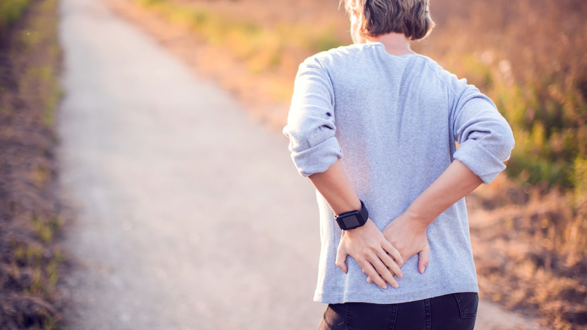 Older woman with a sore back, walking along and holder her back
