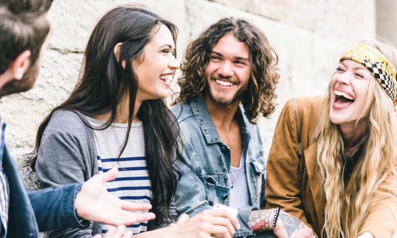 Four friends enjoying each others company and laughing whilst sitting against a building outside
