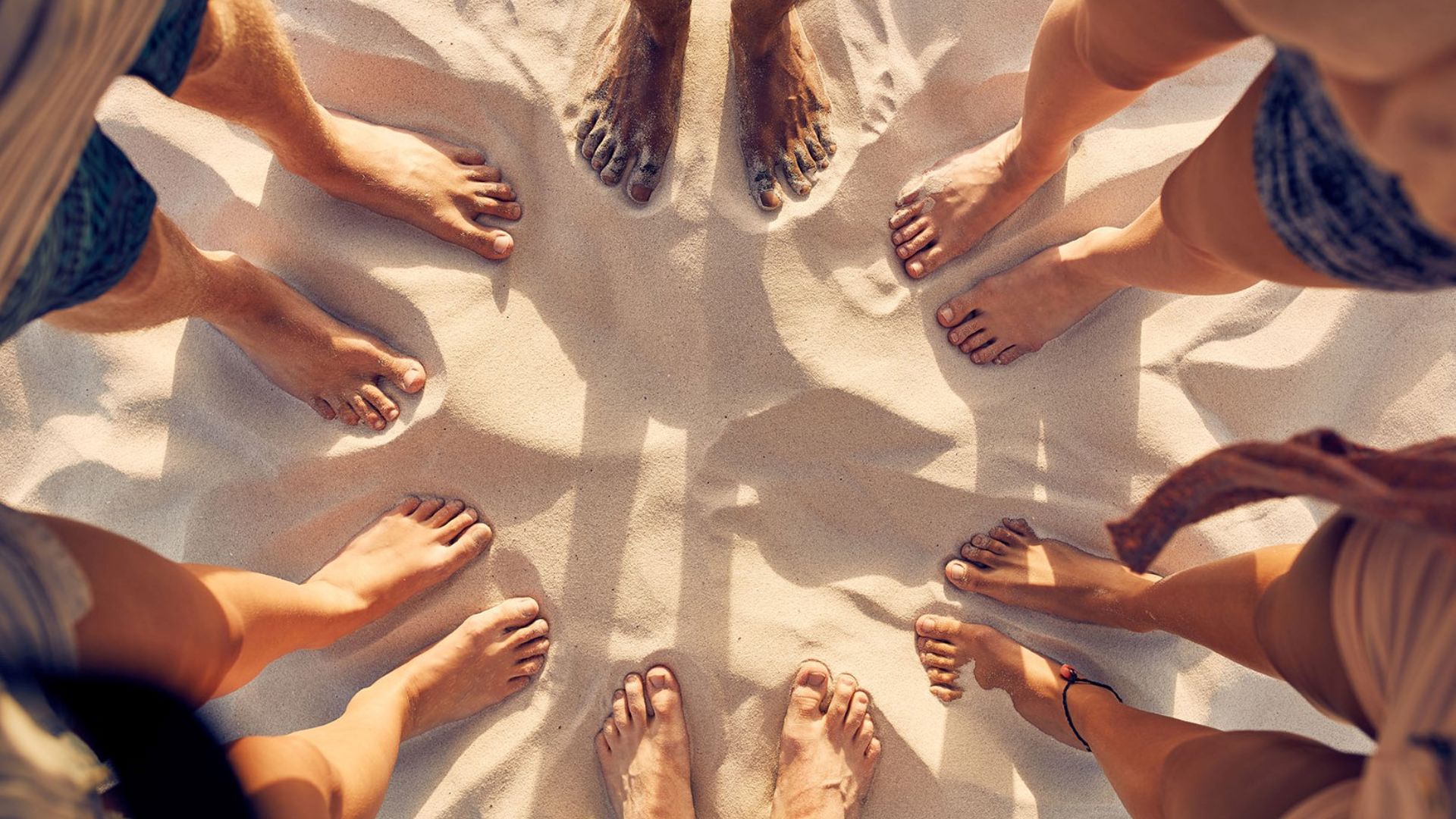 The barefeet of six people standing in a circle at the beach in summer. 