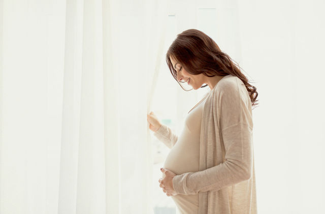 Pregnant woman standing by the window cradling belly