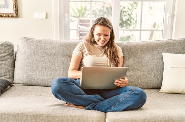 girl in late 20s sitting on the couch using a laptop to research GMHBA Hospital cover