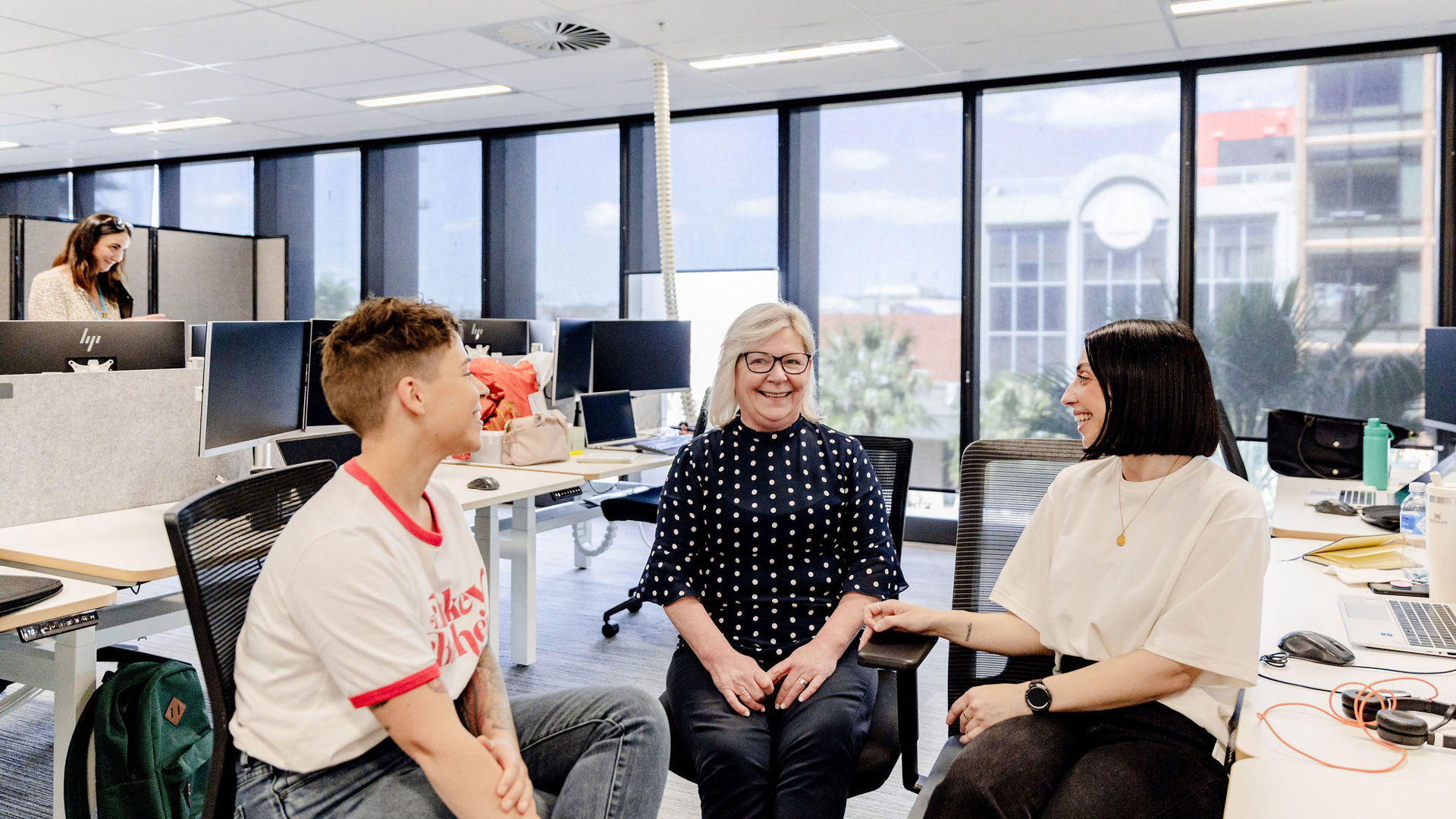 Three GMHBA Staff members happily chatting in light filled open office space