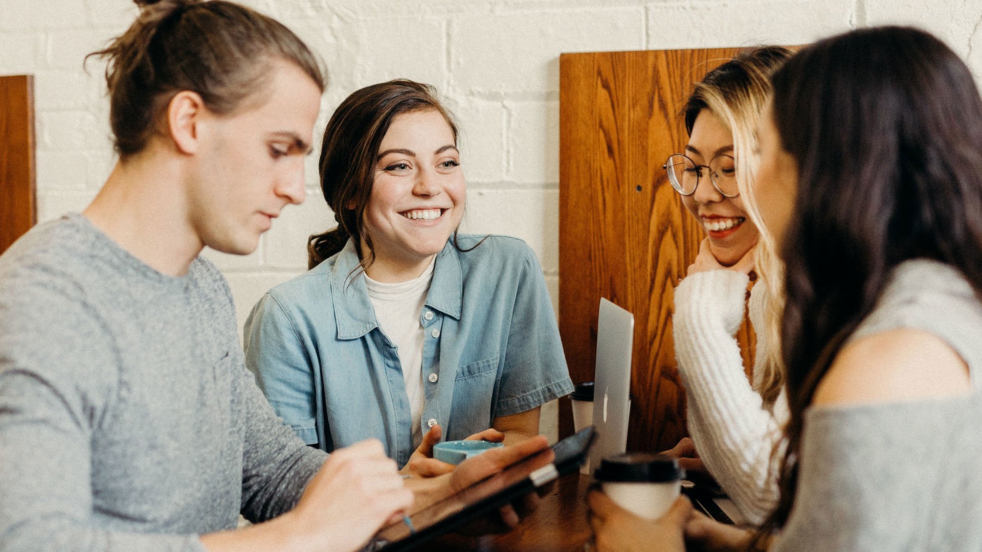 Four young adults smiling and drinking coffee one male is checking a device